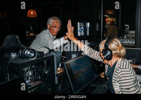 Male and female friends doing high five while playing computer game in gaming center Stock Photo