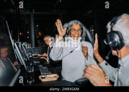 Happy senior couple giving high-five while winning video game at gaming center Stock Photo