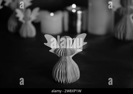 DIY paper angel on a dark background. Religious symbols, festive Christmas and New Year decor. Black and white artistic low key photo. Burning candles Stock Photo