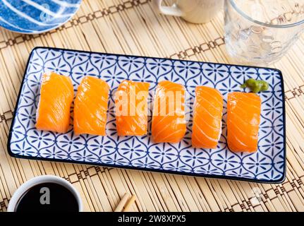Blue rectangular ceramic plate of delicious salmon nigiri with soy souse on bamboo mat. Stock Photo