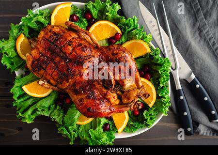Christmas Roast Duck With Cranberry-Orange Glaze: Roasted and glazed whole duck on a garnished platter with carving knife and fork Stock Photo