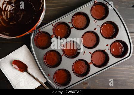 Muffin Pan Filled with Chocolate Cupcake Batter in Paper Cups: Unbaked chocolate cupcakes in a non-stick muffin tin with paper paper liners Stock Photo