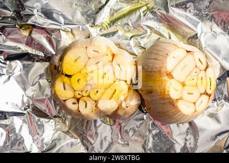 Raw Garlic Bulbs Drizzled with Extra Virgin Olive Oil: Unpeeled and trimmed heads of garlic drizzled with olive oil and sea salt  on aluminum foil Stock Photo