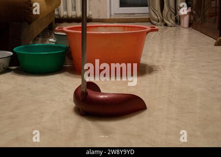 Bowls and pots are on the floor due to water flowing from the ceiling in a flooded apartment due to a burst pipe in the neighbors on the top floor, fl Stock Photo