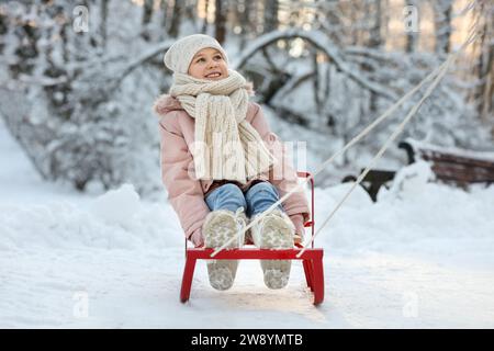 Cute little girl enjoying sledge ride through snow in winter park Stock Photo