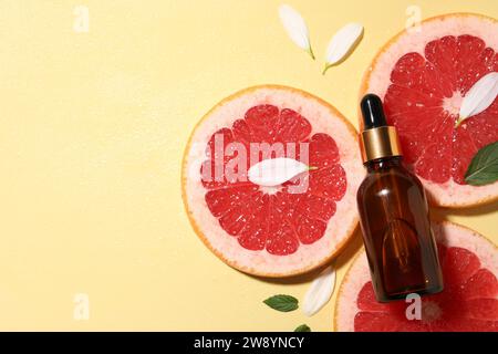 Bottle of cosmetic serum, grapefruit slices and green leaves on wet yellow background, flat lay. Space for text Stock Photo