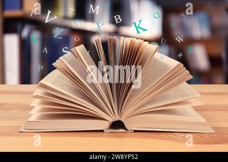Open book with letters flying out of it in library Stock Photo
