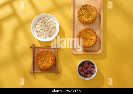 Mid-Autumn Festival decoration ideas in minimalist style. Top view of mooncakes on wooden trays decorated with jams and pumpkin seeds on a yellow back Stock Photo