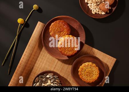 Wooden dishes containing mooncakes and different types nuts decorated on black background. Chinese Mid-Autumn Festival concept made from mooncakes, te Stock Photo