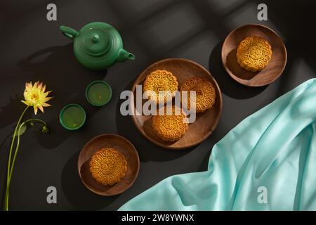 Overhead view of wooden dishes containing mooncakes decorated with green tea set, yellow flower and blue silk cloth. Background of Chinese Traditional Stock Photo