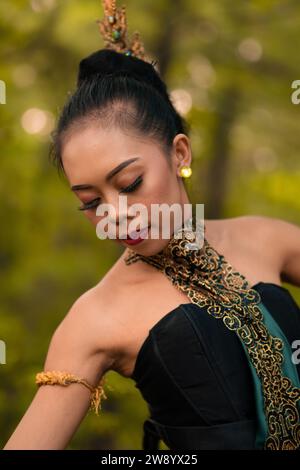 Portrait of a beautiful Asian woman in makeup while dancing in front of the jungle with a black and green costume on her body during the daylight Stock Photo