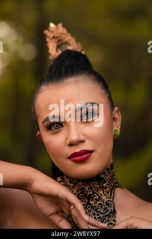 Beautiful eyes of an Asian woman in makeup and red lipstick while wearing gold jewelry and black hair while standing in front of the jungle Stock Photo