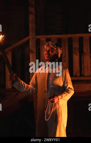 An Arabian man holding a fire torch in the front of a wooden house in the dark night Stock Photo