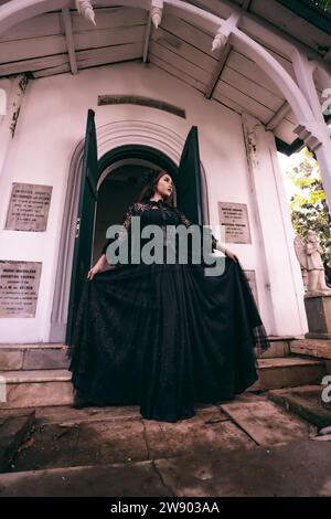 a witch in an all black dress walks down the steps of a cemetery after visiting her deceased brother in the morning Stock Photo