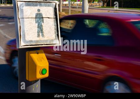 Button to request a green traffic light for pedestrians, while a red vehicle is passing in the background Stock Photo