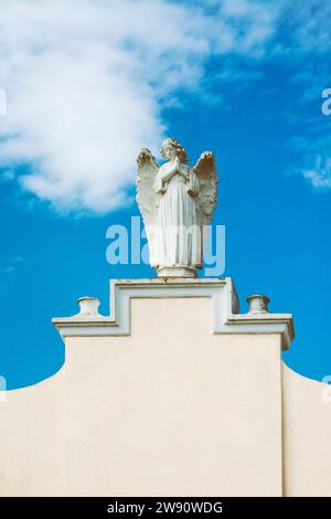 Female sculpture of an praying angel on a white wall with copy space, with blue sky with clouds in the background Stock Photo