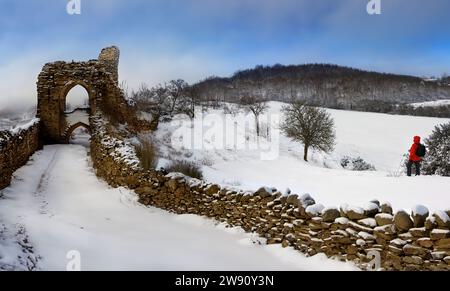 A walker on a snow covered hillside near the ruins of a castle in the Highlands of Scotland. Stock Photo
