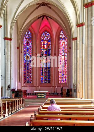 Woman sitting and praying in the church full of light and pink reflections Stock Photo