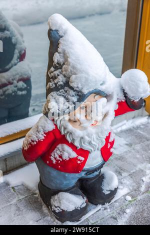 Beautiful view of a charming gnome figure standing at the entrance door of the villa, covered in snow on a frosty winter day. Stock Photo