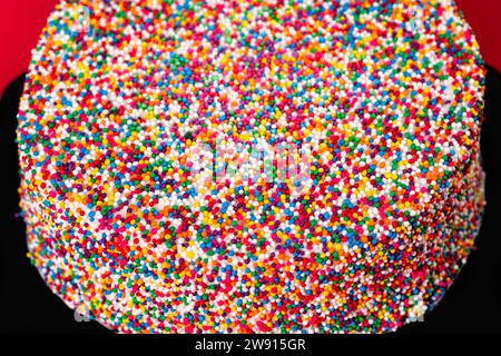 Close-up shot of white icing cake encrusted in multi-colored sprinkles. Celebration concept. Selective focus. Stock Photo