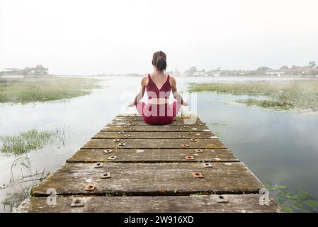 Woman meditating on jetty by lake or river, rear view, mist and fog in the early morning Stock Photo
