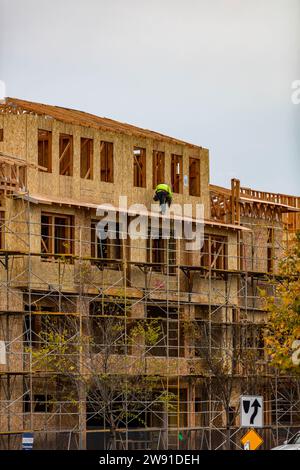 A construction worker working on a side of a framed building during construction Stock Photo