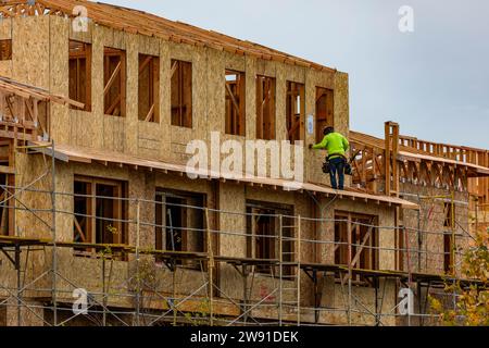 A construction worker working on a side of a framed building during construction Stock Photo