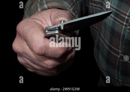 A man's hand opens a dangerous one-handed knife. These are illegal in Germany. Warning of legal consequences. Stock Photo