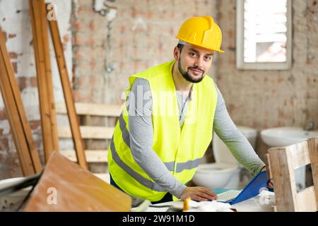 Smiling young engineer checking house renovation plan on laptop Stock Photo