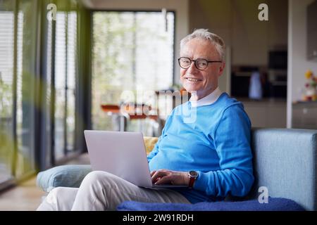 Smiling senior man using laptop on couch at home Stock Photo