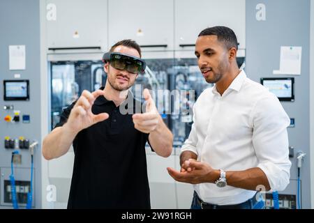 Technician wearing augmented reality glasses in a factory interacting with colleague Stock Photo