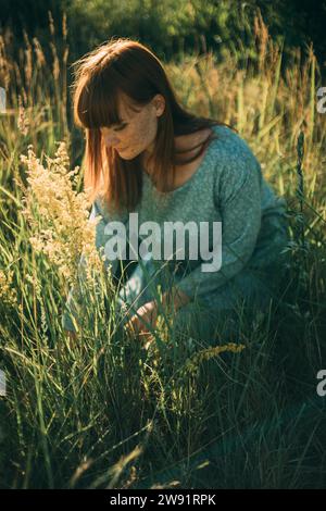 Young redhead woman kneeling in meadow Stock Photo
