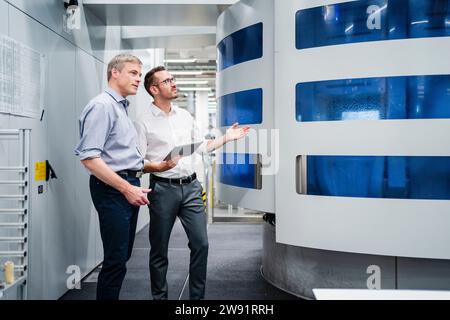 Two businessmen with digital tablet looking at machine in a factory Stock Photo