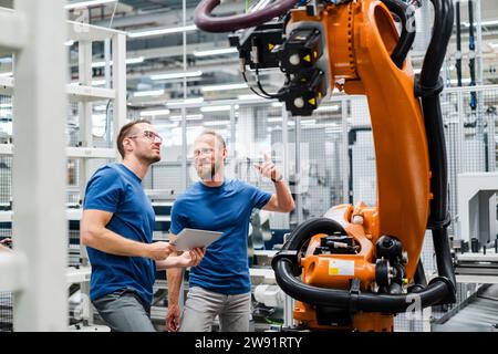 Two technicians with digital tablet examining industrial robot in a factory Stock Photo