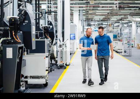 Two colleagues walking and sharing digital tablet in a factory Stock Photo