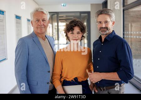 Smiling businessmen standing with colleague in office corridor Stock Photo