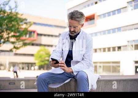 Doctor using smart phone in front of building Stock Photo