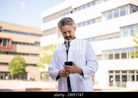 Doctor using mobile phone in front of buildings Stock Photo