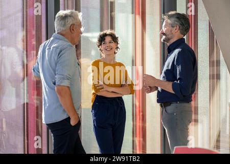 Smiling businesswoman talking to colleagues near window Stock Photo