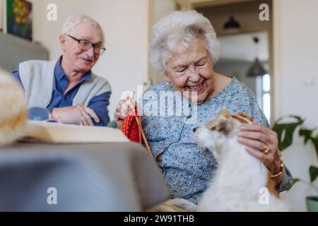 Happy senior woman stroking dog with man sitting at table Stock Photo