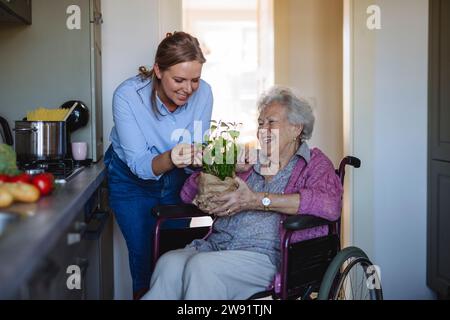 Smiling senior woman with healthcare worker touching plant leaves Stock Photo
