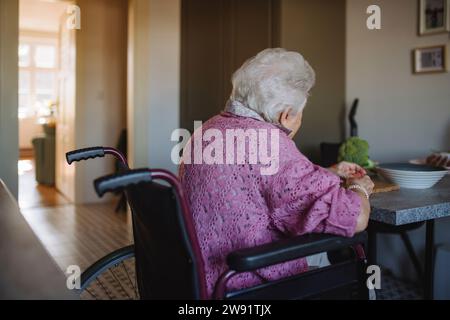 Senior woman sitting in wheelchair at table Stock Photo