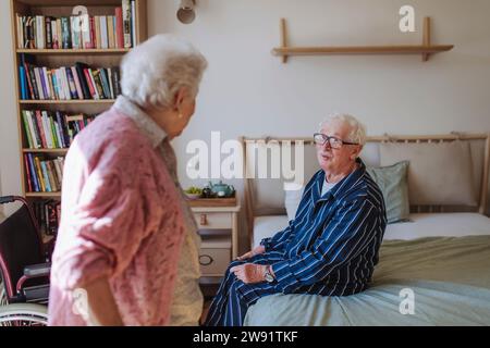 Senior woman talking with man sitting on bed at home Stock Photo