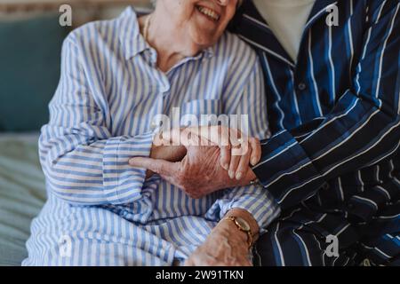 Happy senior woman holding hands with man sitting on bed at home Stock Photo