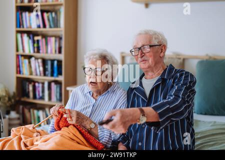 Senior woman knitting with man holding remote and watching TV at home Stock Photo