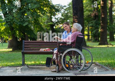 Happy healthcare worker with senior woman sitting in wheelchair at park Stock Photo