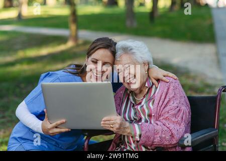 Smiling healthcare worker with senior woman using laptop in park Stock Photo