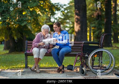 Healthcare worker with senior woman reading newspaper in park Stock Photo