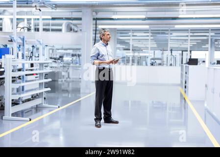 Thoughtful engineer with tablet PC standing at factory Stock Photo