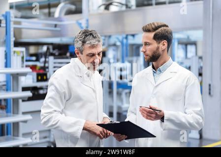 Engineers wearing lab coat and discussing over clipboard in factory Stock Photo